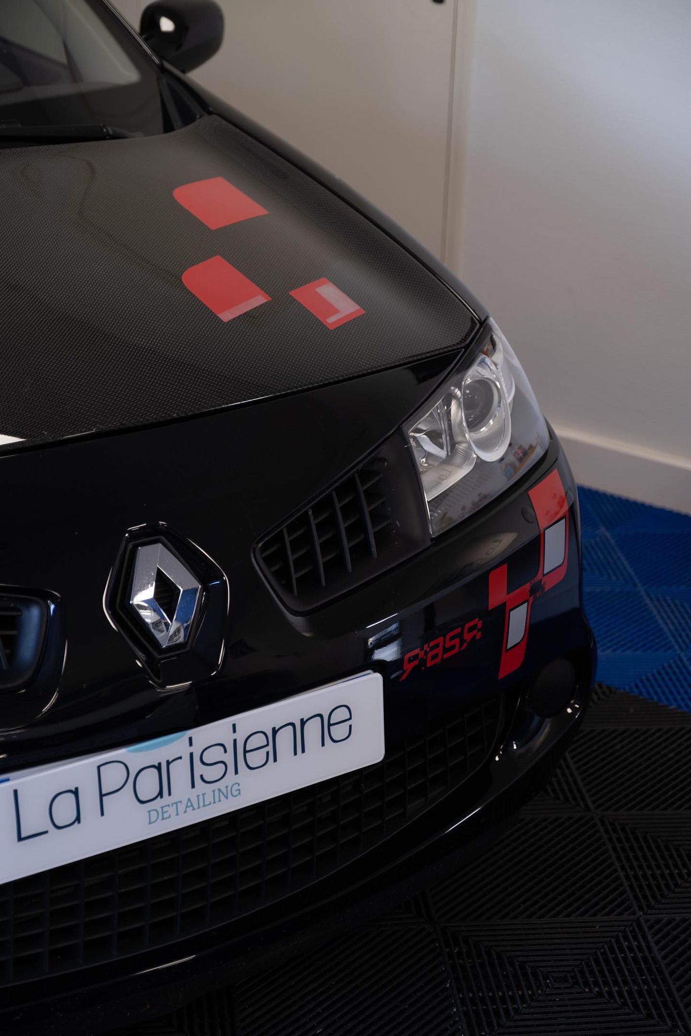Voiture de couleur noir et rouge de marque Renault en zoom sur l'avant de la voiture. La voiture est dans un établissement qui fais des nettoyages détaillés de voiture.
